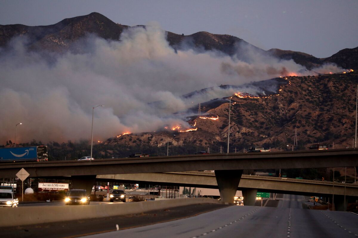 Flames and thick clouds of smoke in the hills can be seen from a freeway in the Saddleridge fire