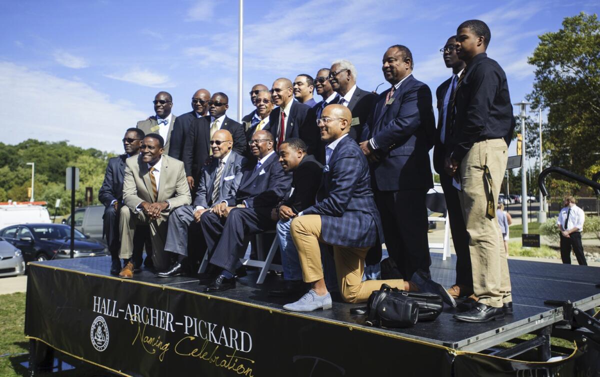 Older and newer generations of Alpha Phi Alpha fraternity pose for a photograph on a stage.