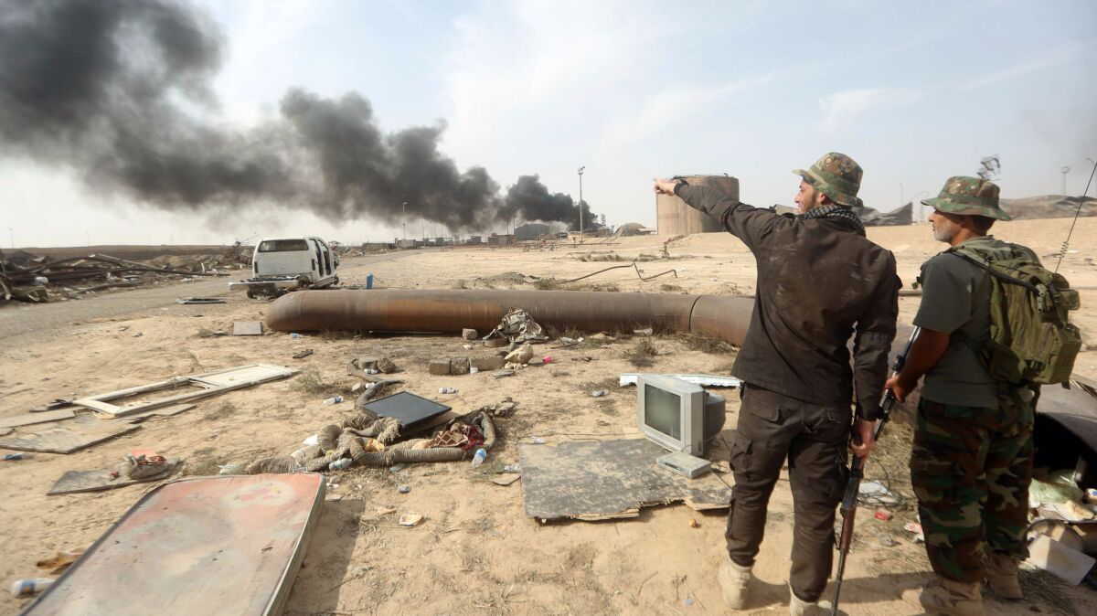 Iraqi fighters look at the damage Oct. 17, 2015, after security and allied paramilitary forces recaptured a refinery complex from Islamic State extremists in Baiji.