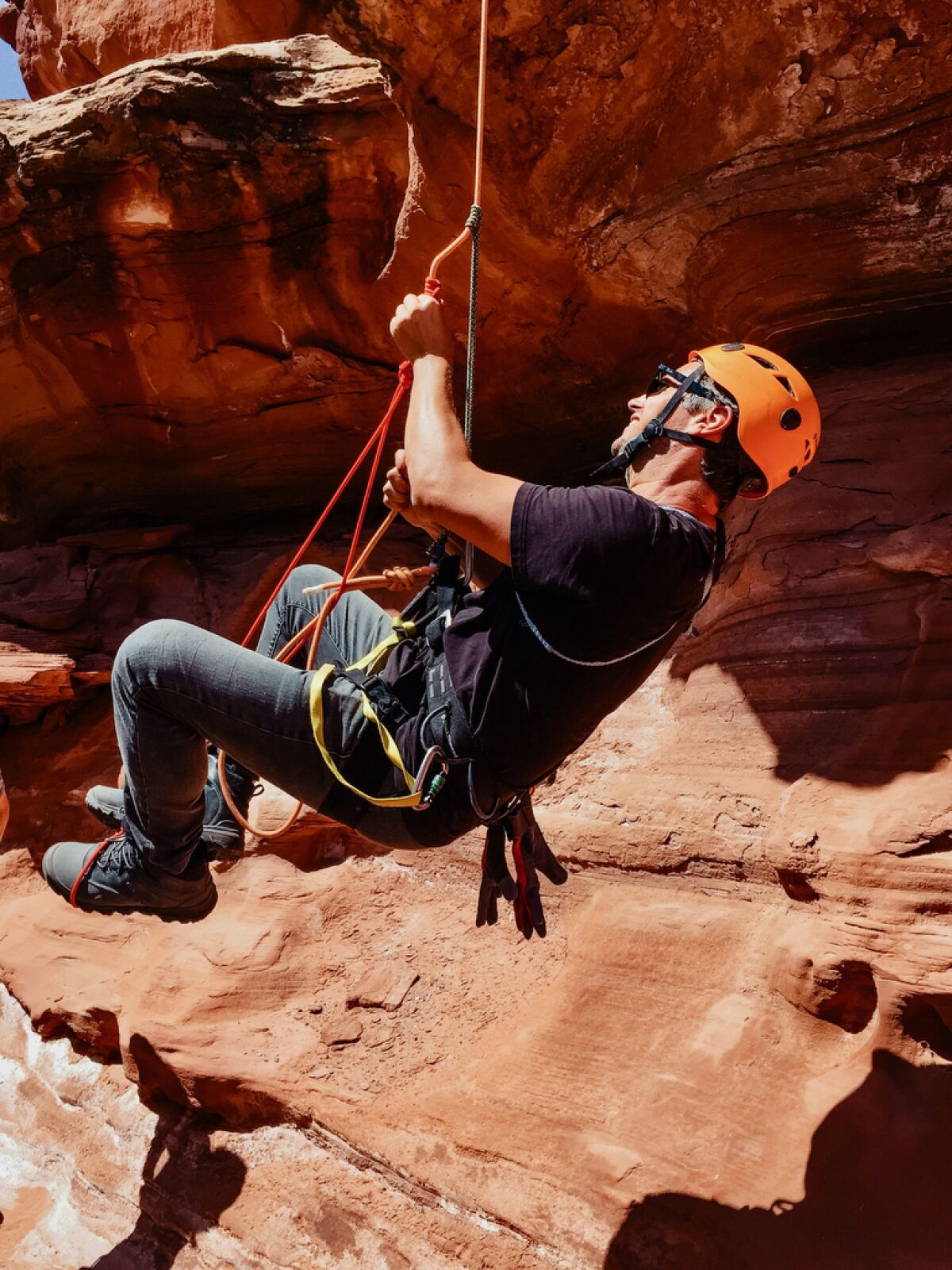 A man hangs from a rope under a rocky ledge