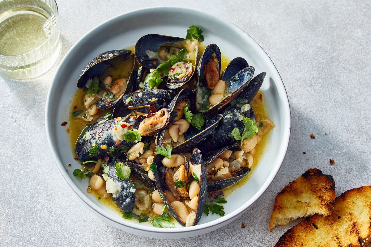 Steamed mussels in a dish with white beans and herbs.