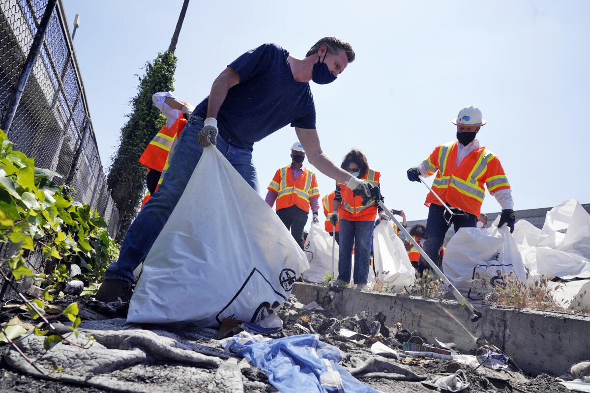 FILE - In this Tuesday, May 11, 2021, file photo, California Gov. Gavin Newsom joins a cleanup effort in Los Angeles. Newsom on Tuesday proposed $12 billion in new funding to get more people experiencing homelessness in the state into housing and to "functionally end family homelessness" within five years. A fading coronavirus crisis and an astounding windfall of tax dollars have reshuffled California's emerging recall election, allowing Democratic Gov. Newsom to talk of a mask-free future and propose billions in new spending for schools and businesses as he looks to fend off Republicans who depict him as a foppish failure. (AP Photo/Marcio Jose Sanchez, File)