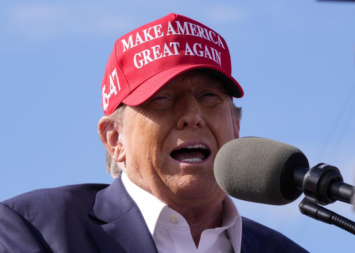 Donald Trump, in a red MAGA hat, speaks at an outdoor rally 