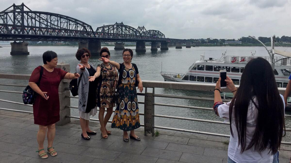 Chinese tourists pose alongside the Yalu River in Dandong, China, with North Korea in the background.