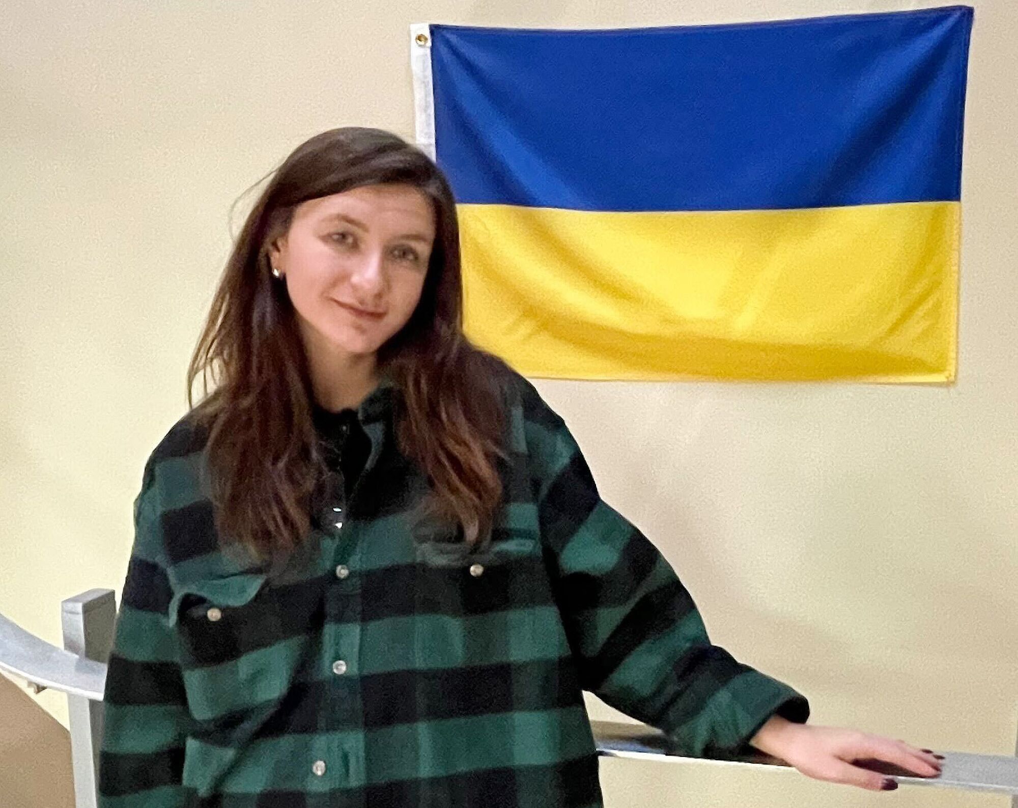 A woman stands near a Ukrainian flag mounted on a wall