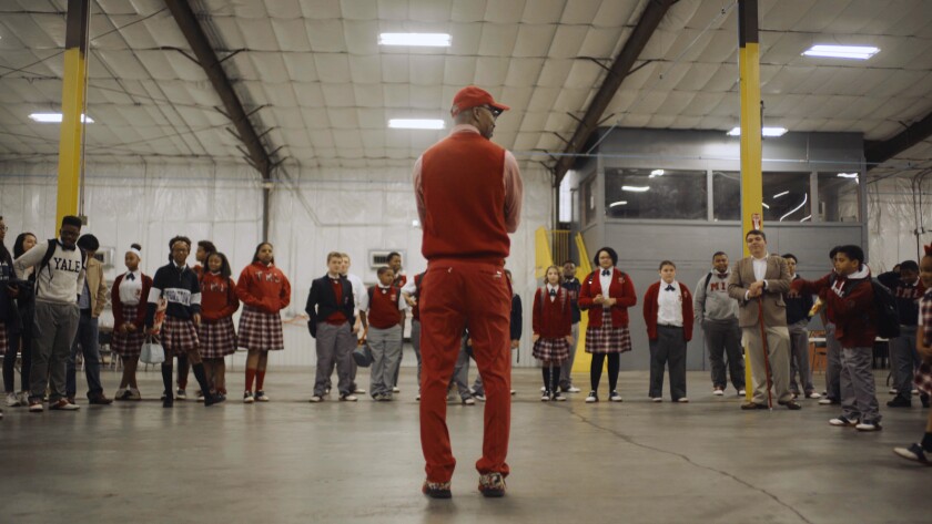 A man in a red cap stands in front of a row of uniformed schoolchildren.