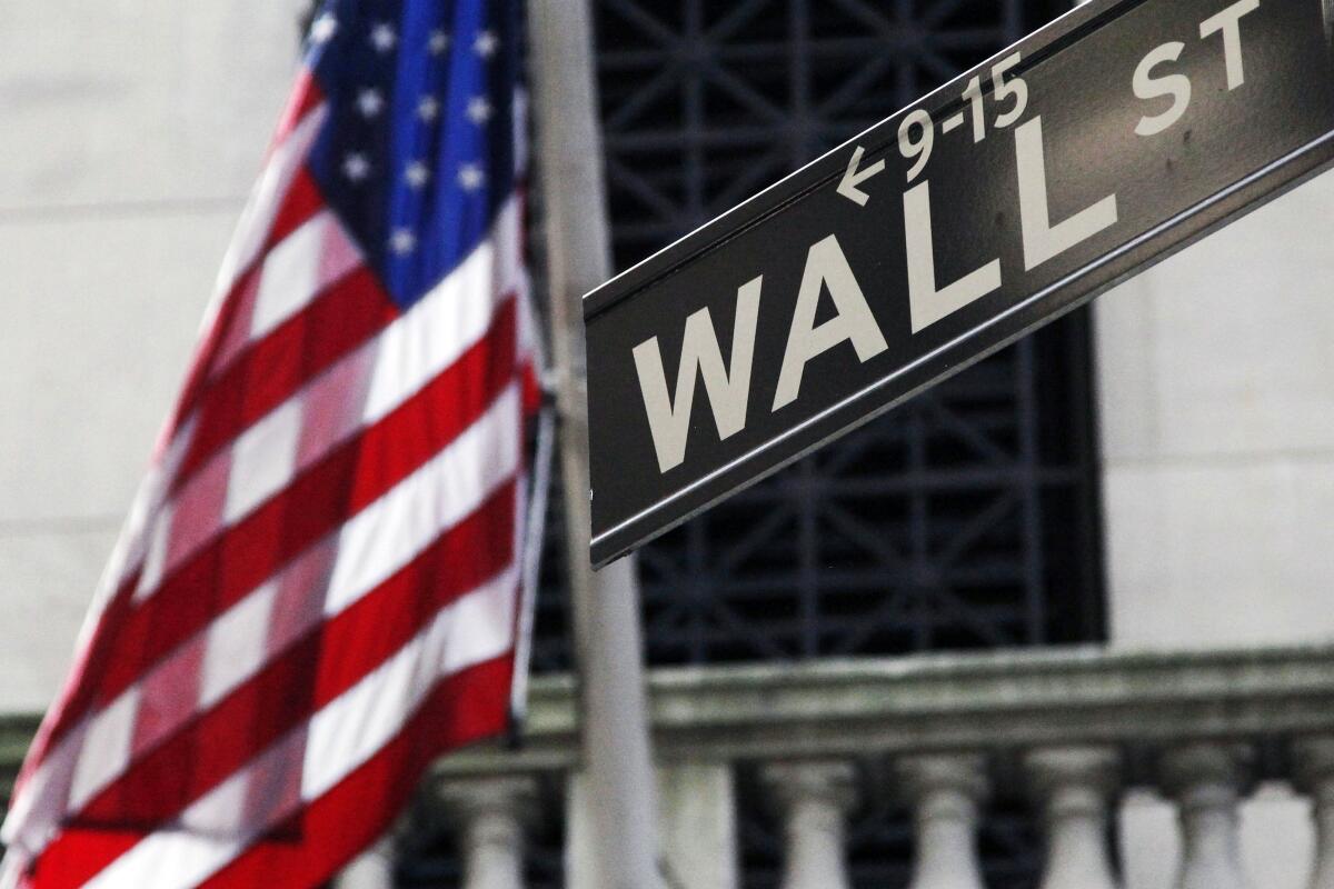 An American flag is to the left of a Wall Street sign.