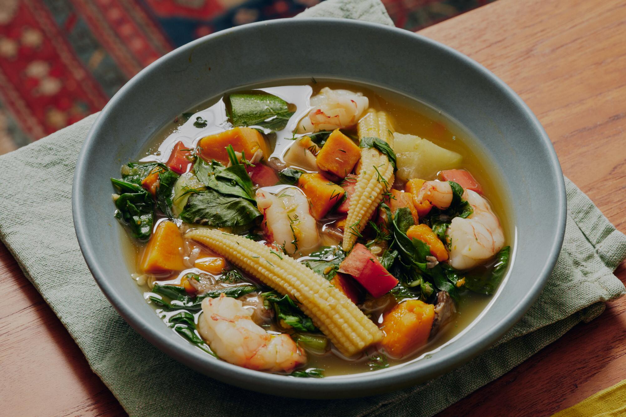 A bowl of soup filled with shrimp and vegetables including carrots and baby corn