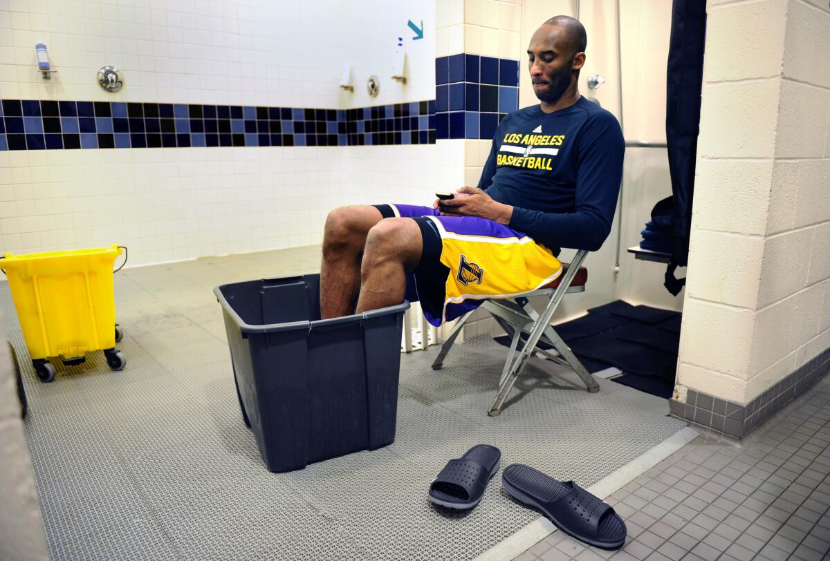 Kobe Bryant checks his phone as he soaks his feet in a bucket of ice water before a game with the Rockets in Houston.