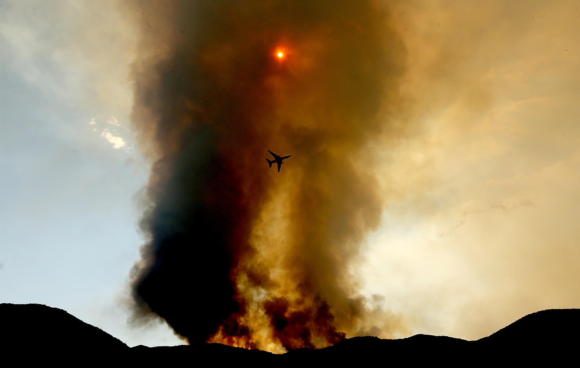 A firefighting jumbo jet is dwarfed by a plume of smoke
