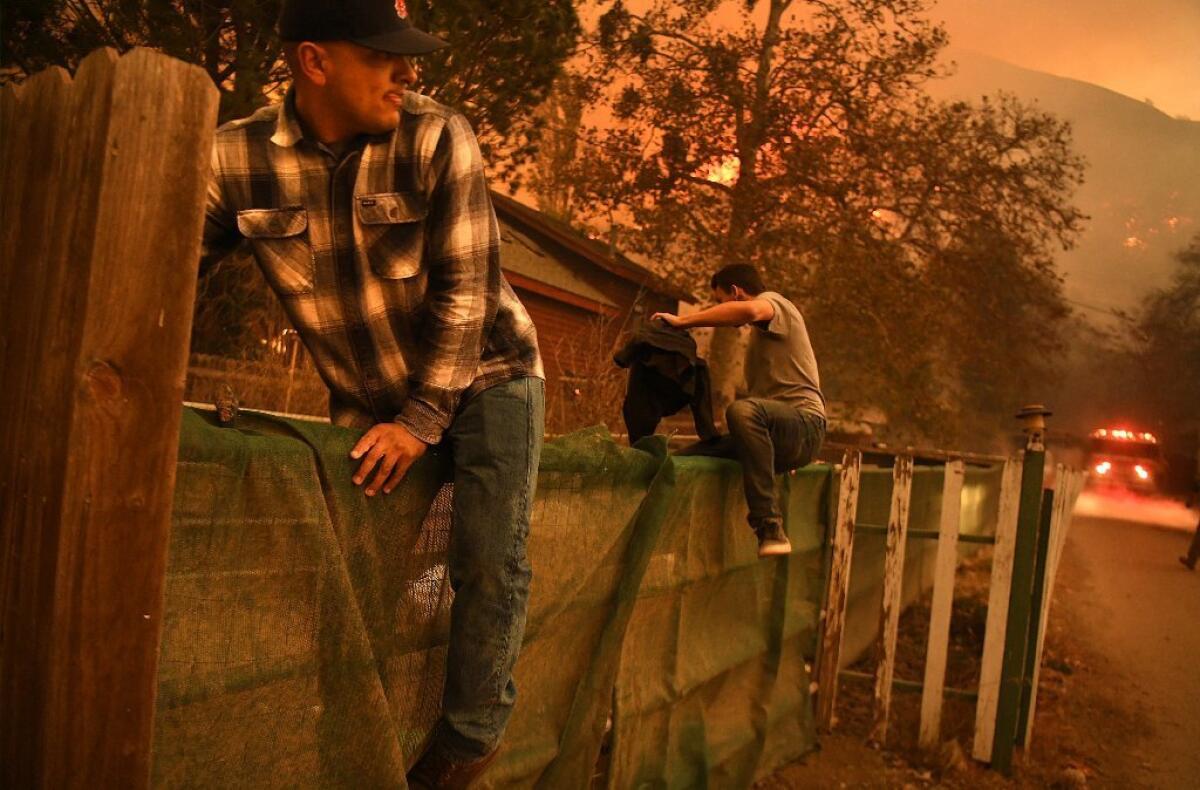 Residents hop a fence Tuesday to put out a spot fire along Highway 33 from the Thomas fire in Casita Springs in Ventura County.