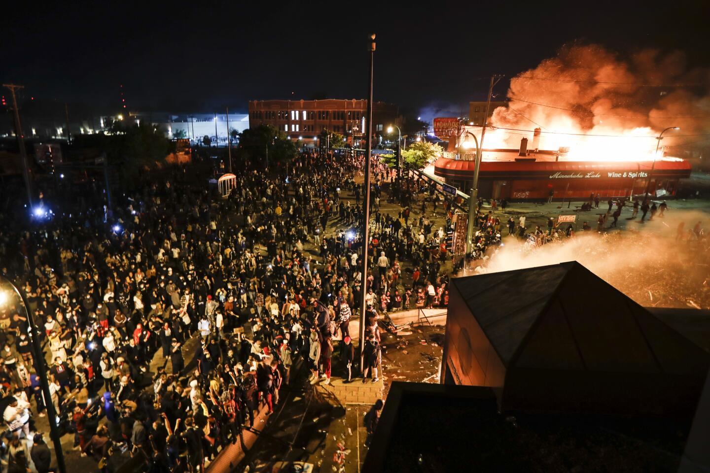 Protesters demonstrate outside the Minneapolis 3rd Police Precinct, which is in flames.