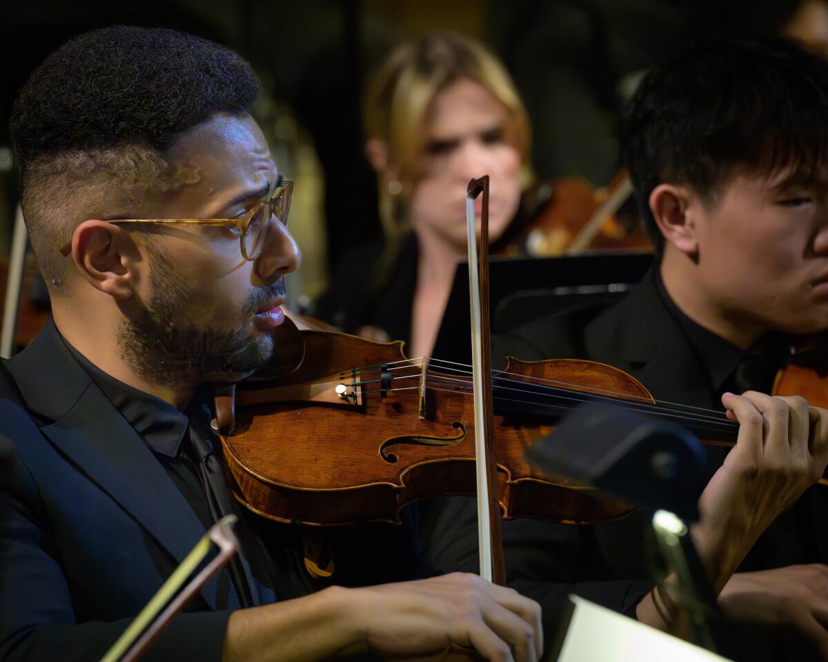 A young man in a black suit plays violin. 