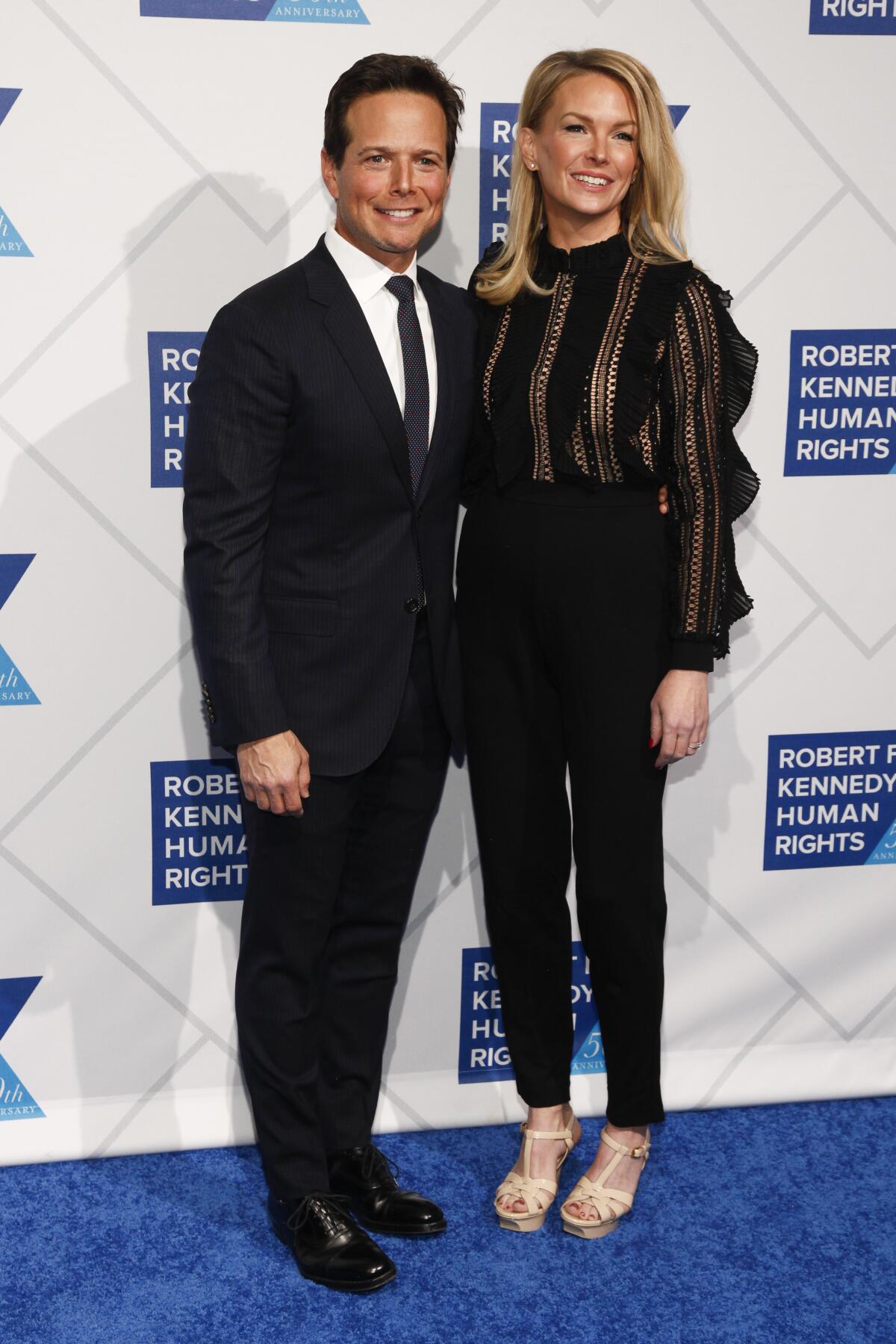 Scott Wolf in a suit and wife Kelley Wolf in pants and a blouse pose for unseen photographers