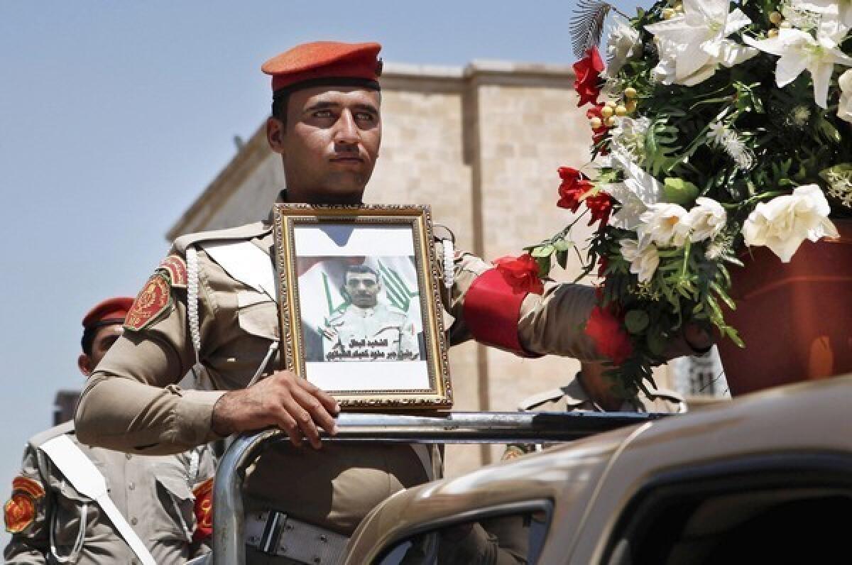 An Iraqi soldier holds a picture of a slain comrade during a Baghdad funeral procession for five soldiers killed by gunmen. Violence has racked the country for a week, prompting the government to shut down TV stations it said were encouraging sectarian conflict.