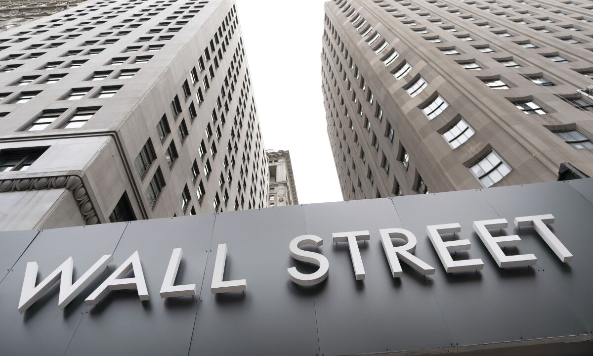 A sign that says "Wall Street" is below high-rise buildings. 