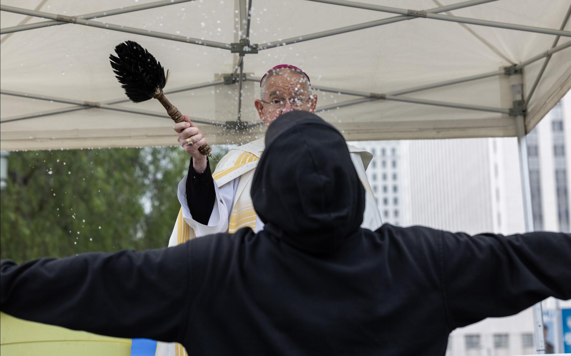 An archbishop splashes water on a man with outstretched arms