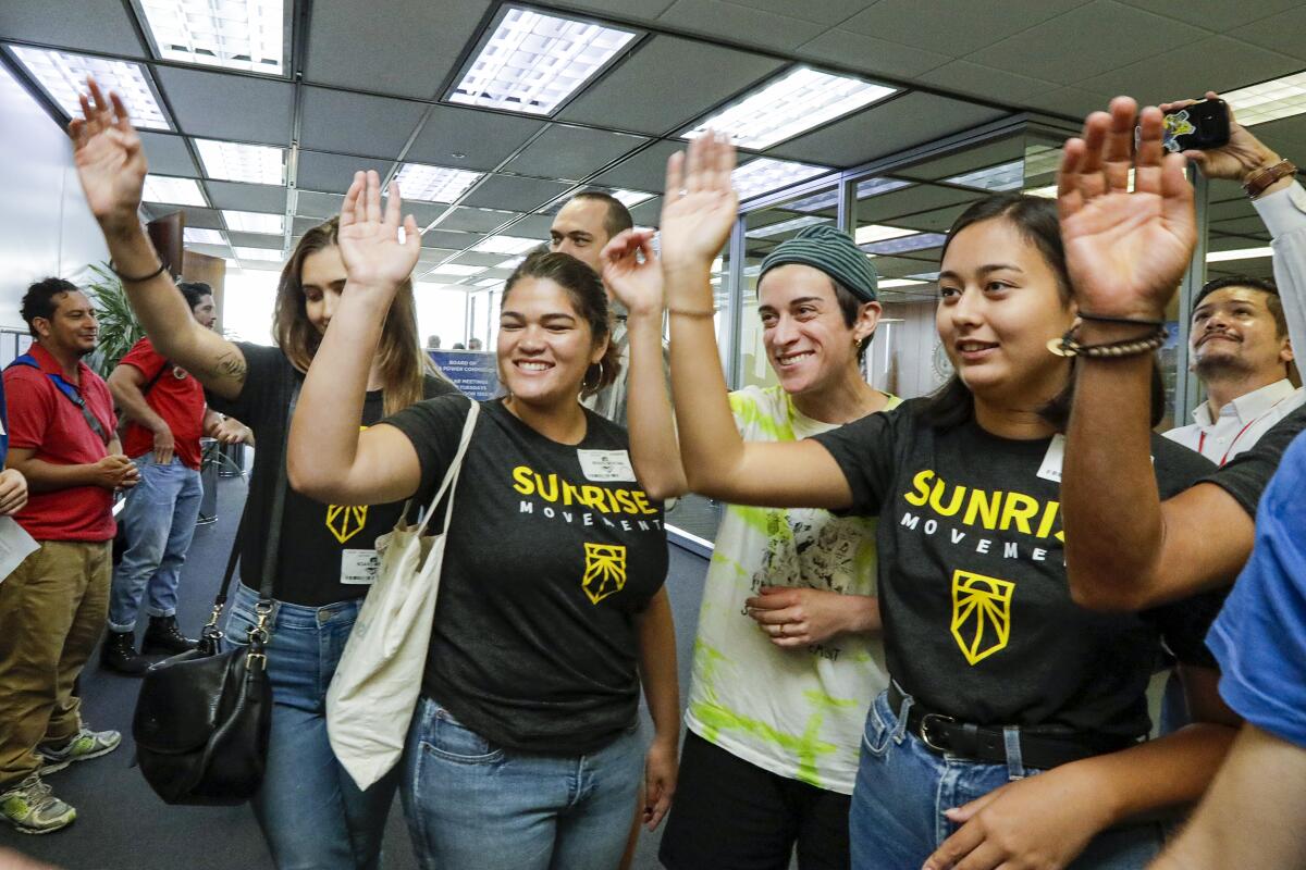 A group of activists, some wearing Sunrise Movement T-shirts, raise their hands in celebration