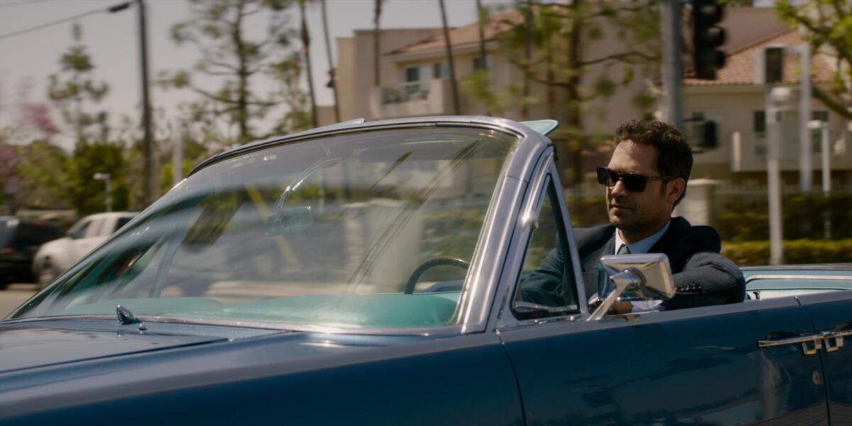 A man in a suit and sunglasses driving a blue convertible in Los Angeles