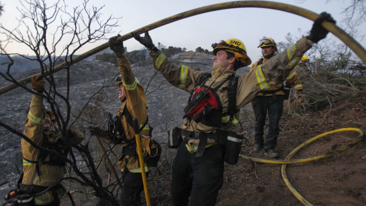 Firefighters work to get a hose over some brush as they manuever on charred hillls.