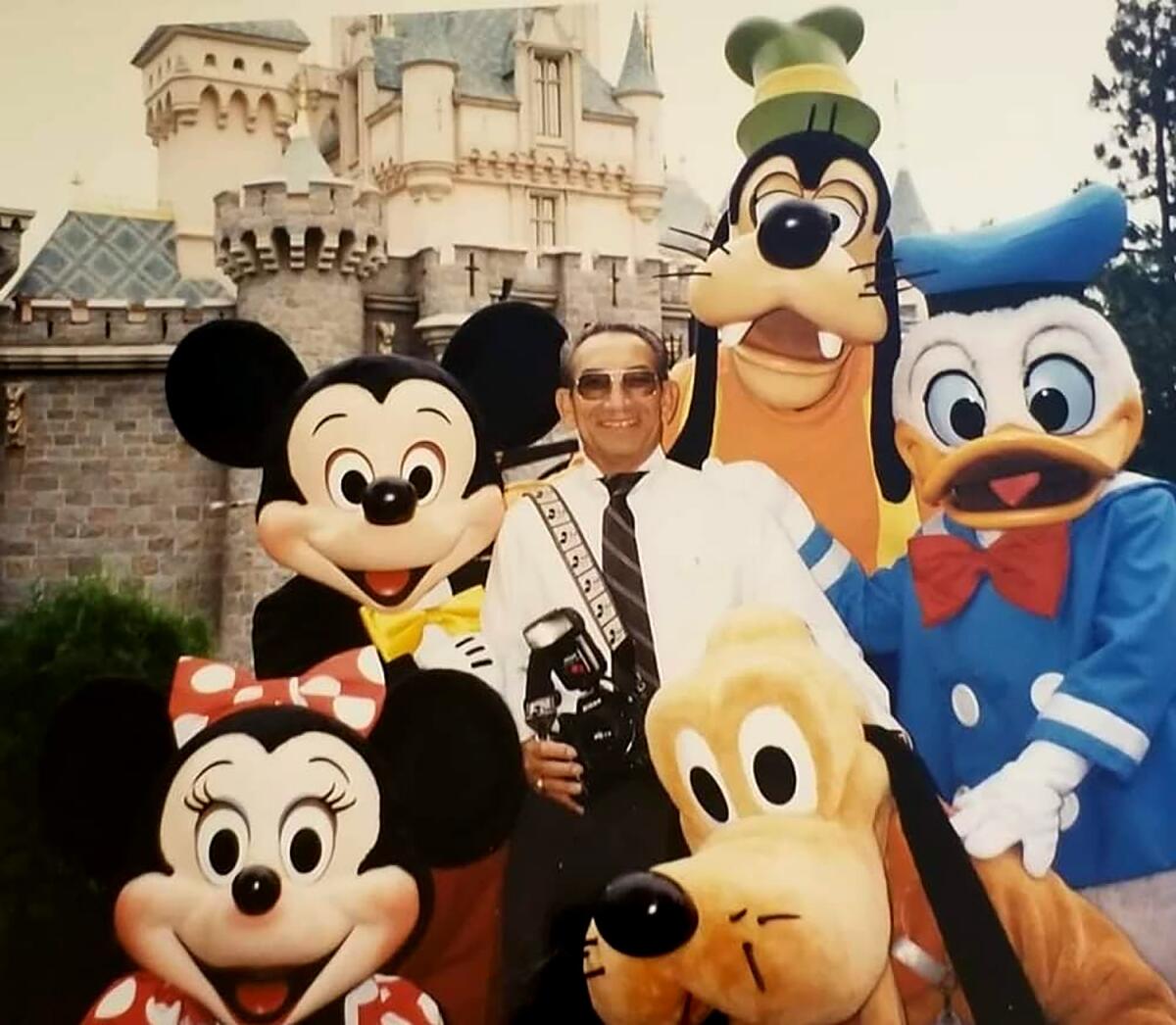 Renie Bardeau, camera strapped over a shoulder, poses with costumed characters at Disneyland.