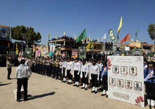 People stand in neat formation, some holding portraits of people and flags