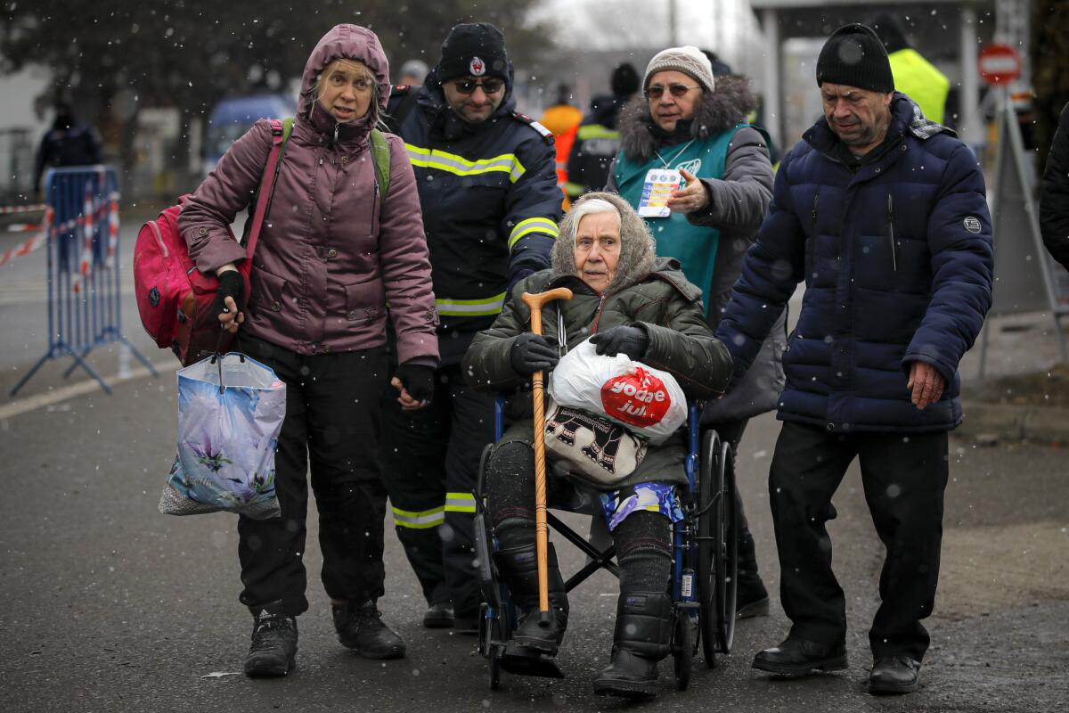 Refugees fleeing the conflict from neighboring Ukraine help push an elderly lady at the Romanian-Ukrainian border