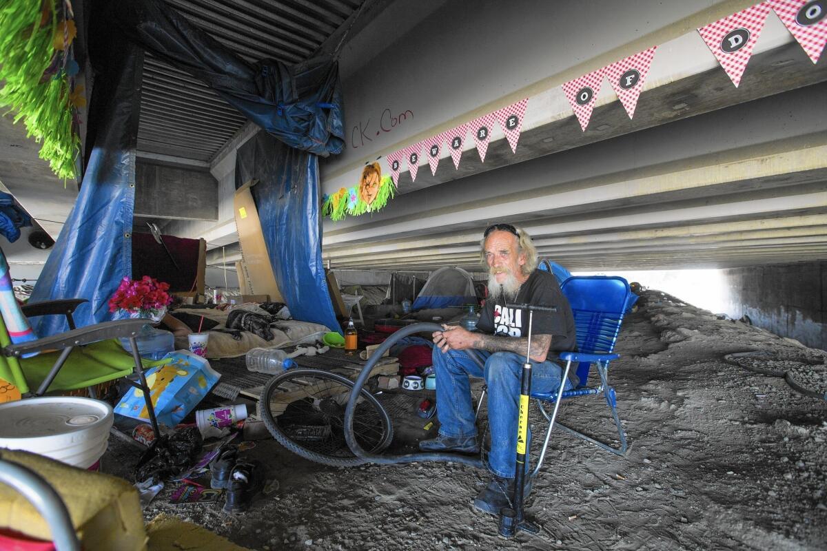 Bill "Tattoo" LeBlanc, de 74 años, repara la cámara de la rueda de su bicicleta, cerca de su campamento en el río Santa Ana, bajo la Autopista 5, en Orange (Allen J. Schaben / Los Angeles Times).