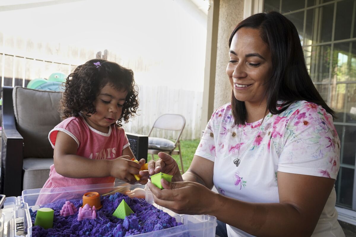 Laura Guerra and her daughter Emilia, 2, play at their home in Riverside, Calif., on Monday, July 11, 2022. California is using some of its record-setting budget surplus to help ease Guerra's mind, and others like her. Last month, California became the first state committed to setting up trust funds for children who lost a parent or caregiver to the pandemic. (AP Photo/Damian Dovarganes)