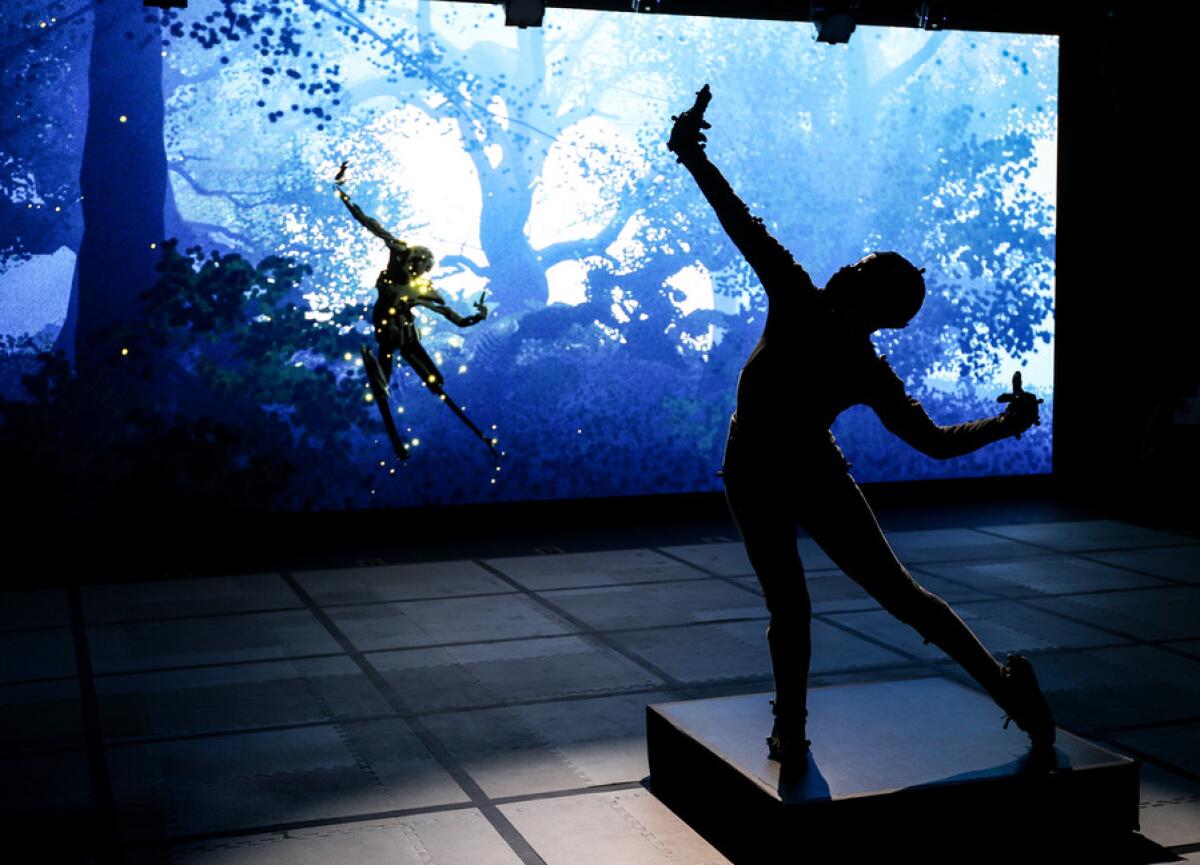 A performer in a capture suit strikes a pose that is projected into a surreal forest projection behind them.