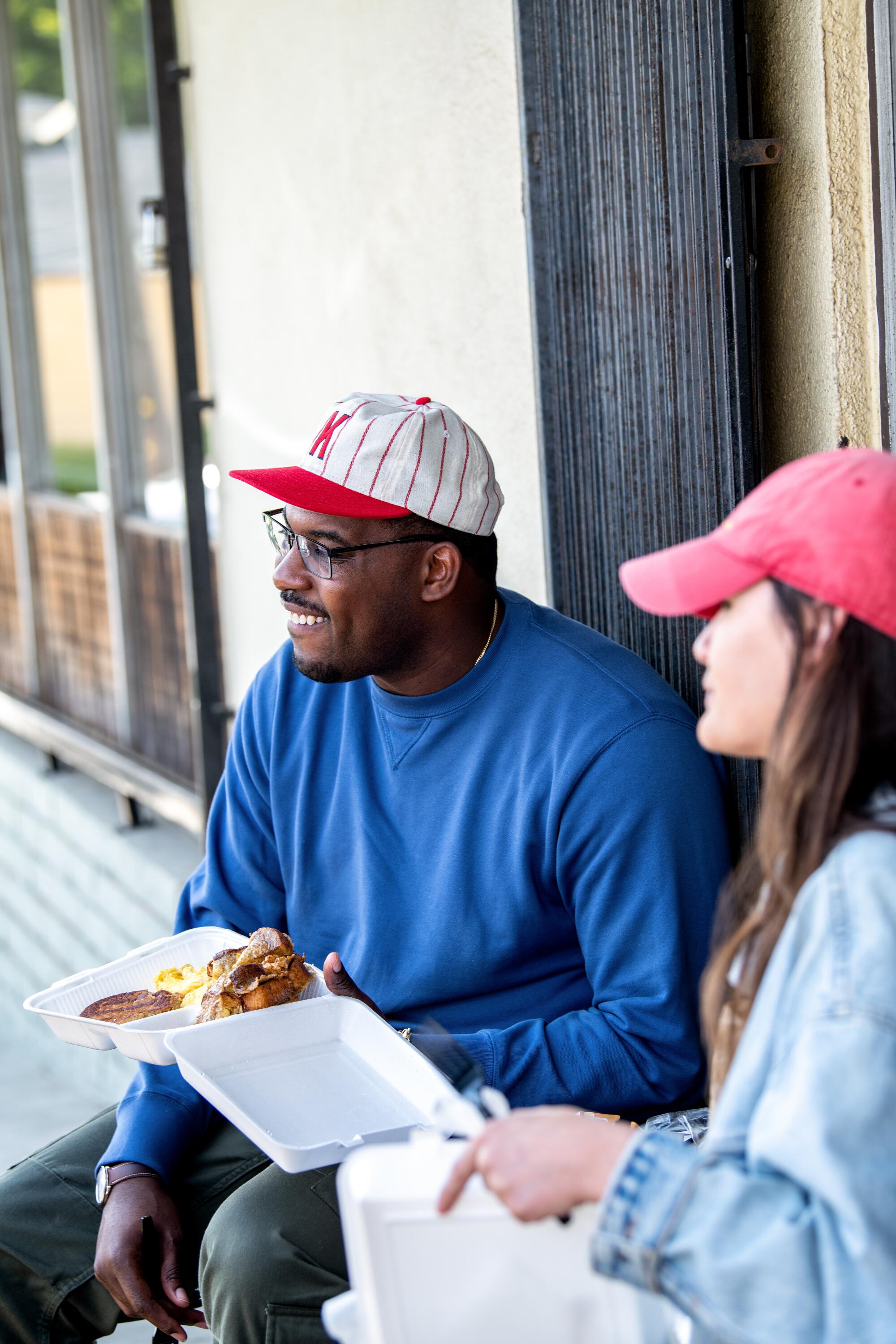 Lionel Boyce and Los Angeles Times food columnist Jenn Harris sit outdoors with takeout food.