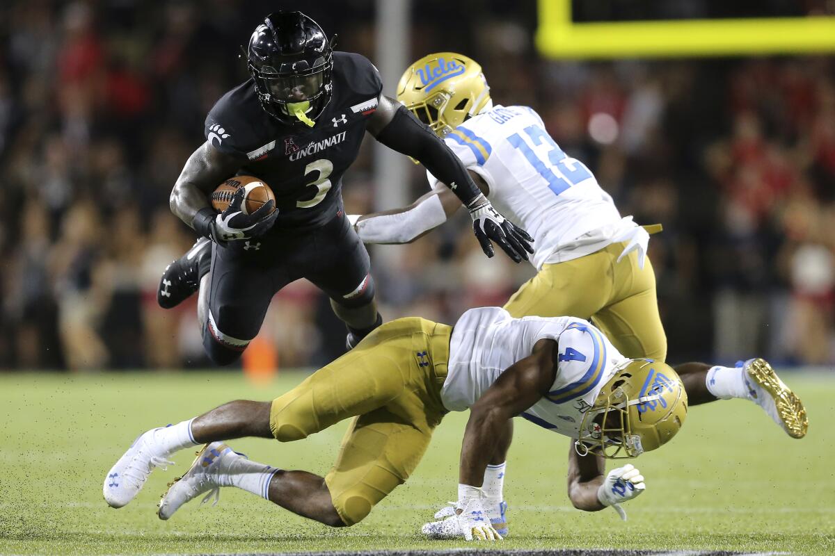 Cincinnati running back Michael Warren II, top left, is upended by UCLA defensive back Stephan Blaylock, bottom.