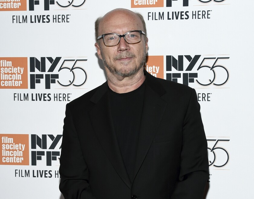 A bald man in glasses and a black suit poses before a New York Film Festival banner.