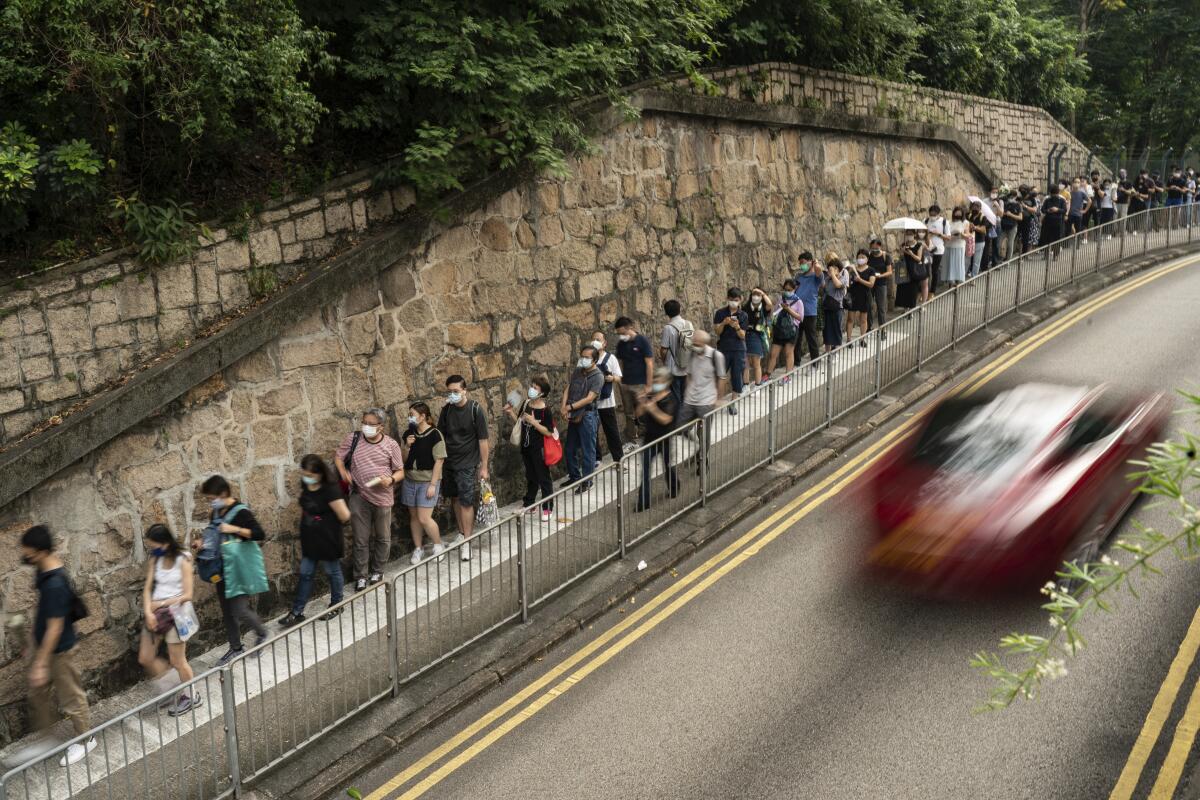 People wait in line while a car drives by.