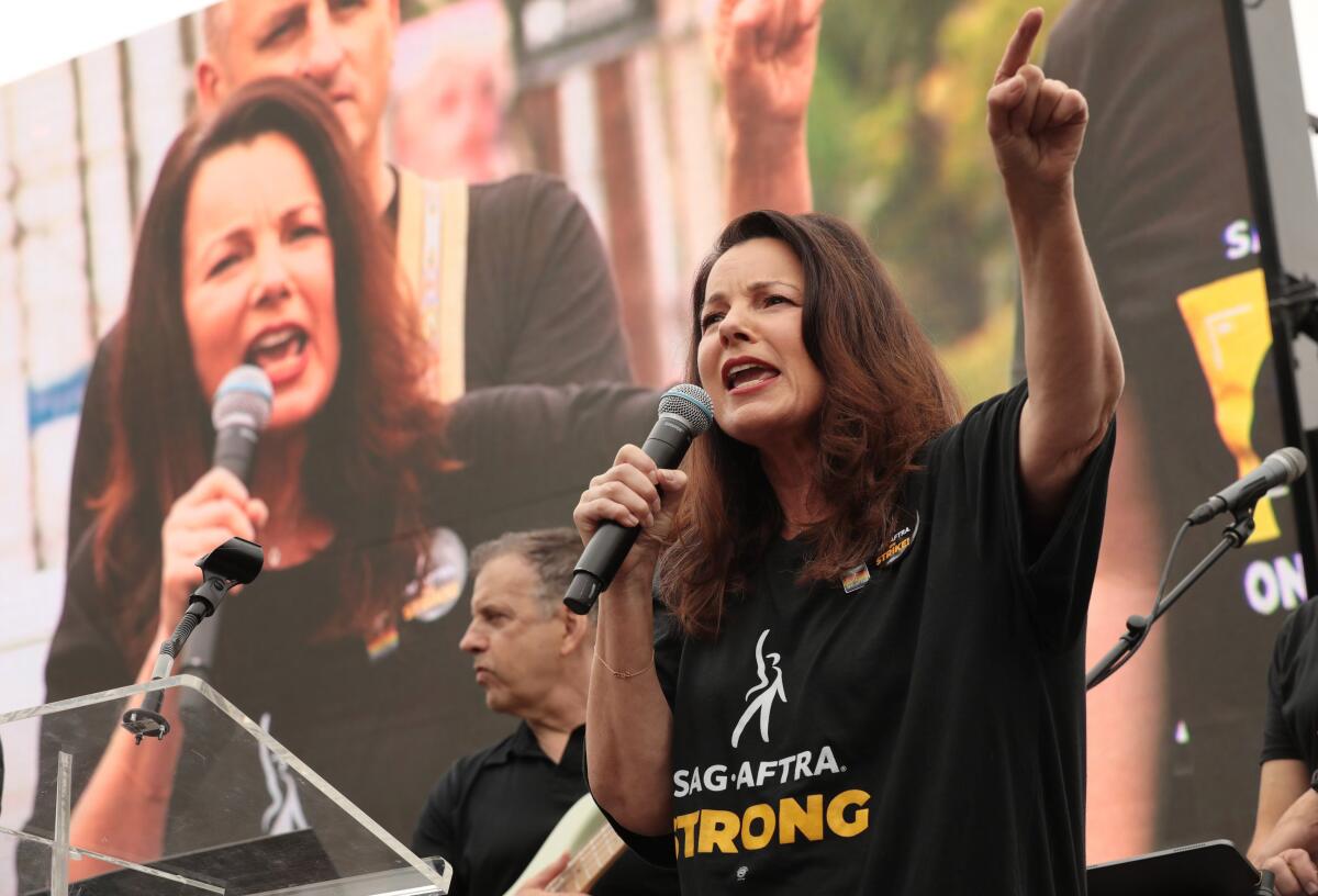 SAG-AFTRA President Fran Drescher speaks into a microphone, her image appearing on the screen behind her.