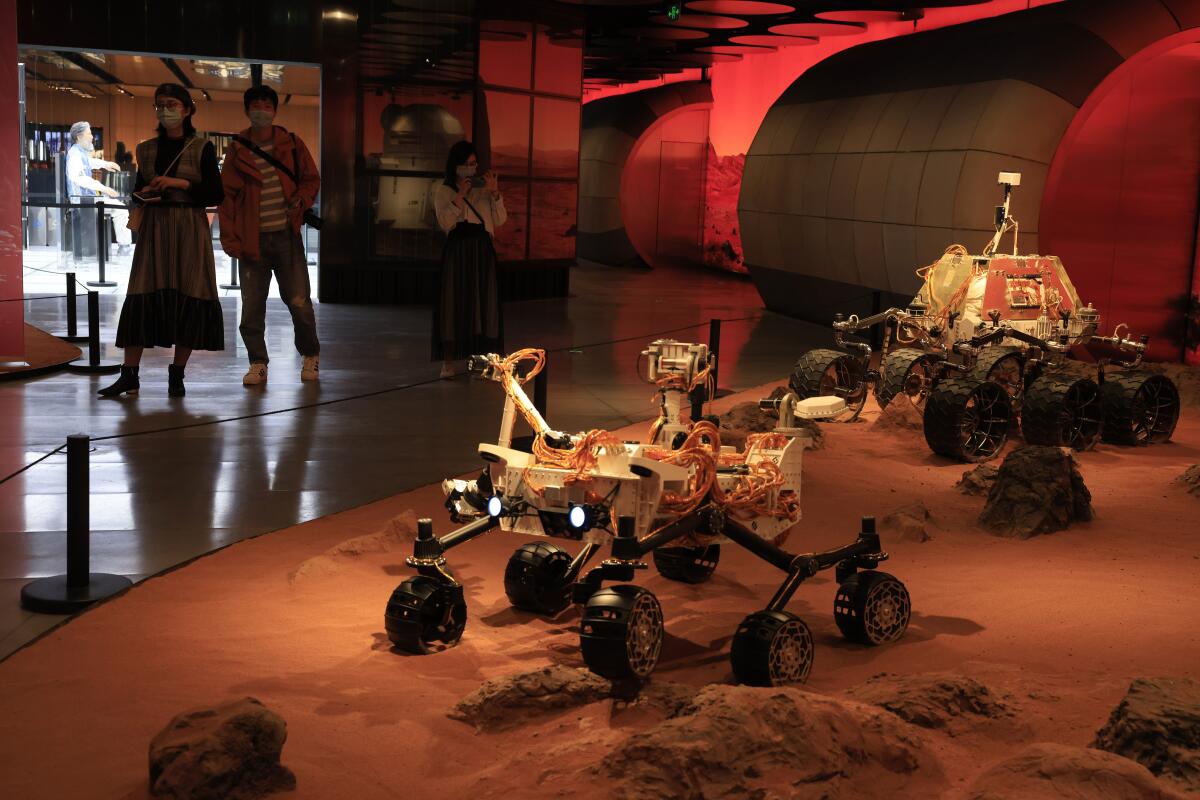 Visitors pass by an exhibition depicting rovers on Mars in Beijing