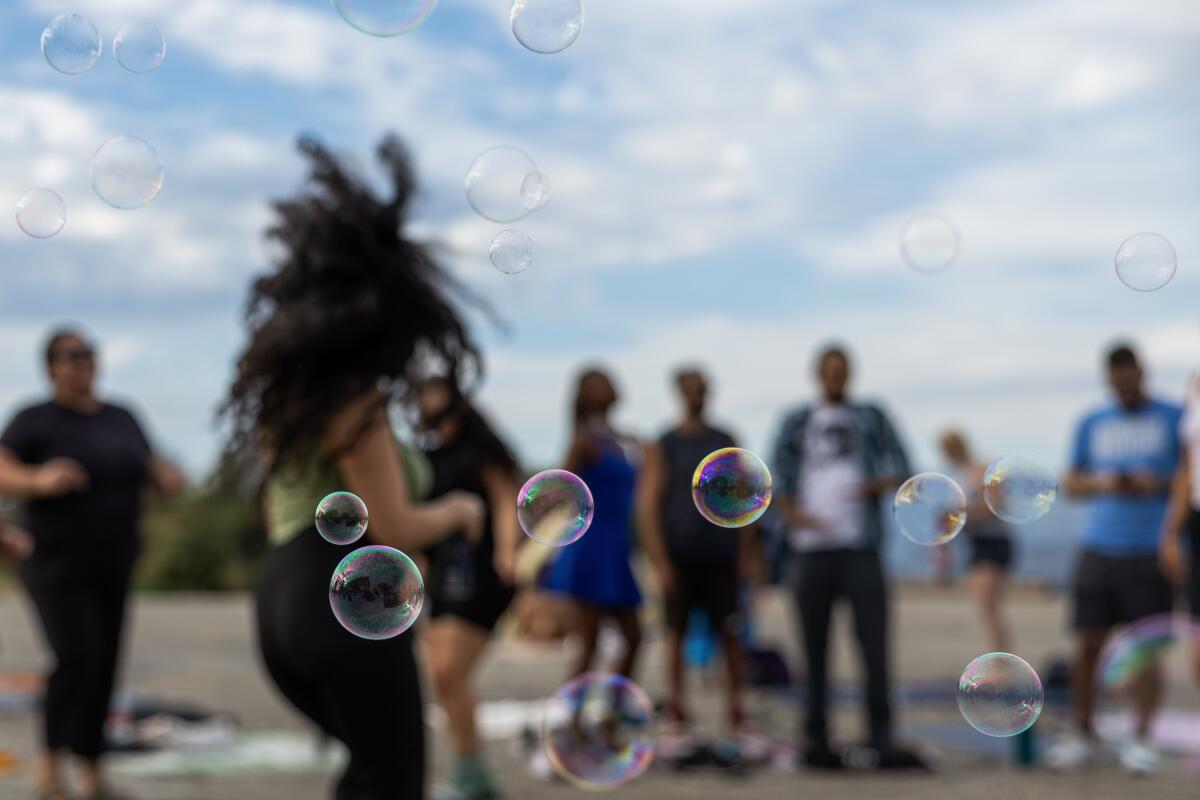 A group of people dance at sunset as bubbles float in the air