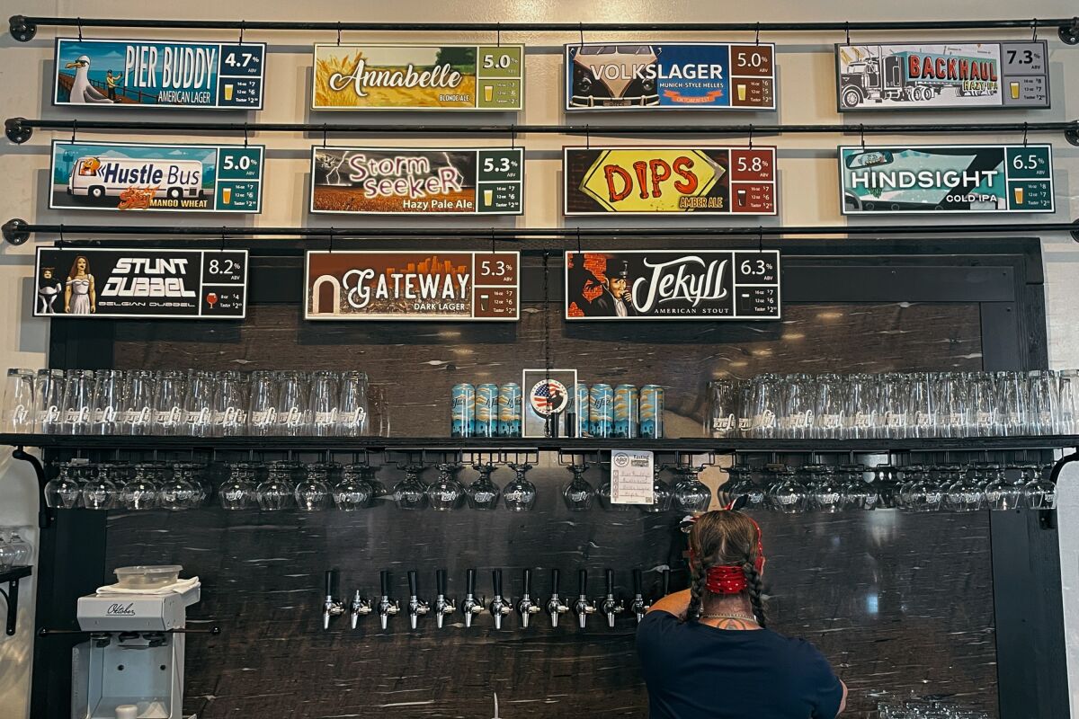 La Jara's menu board on the wall above shelves of cans and glasses and a bartender standing at the taps.