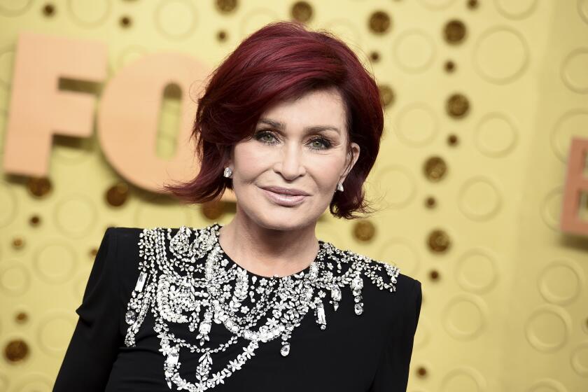 A woman with short red hair wearing a bejeweled black dress in front of a gold background