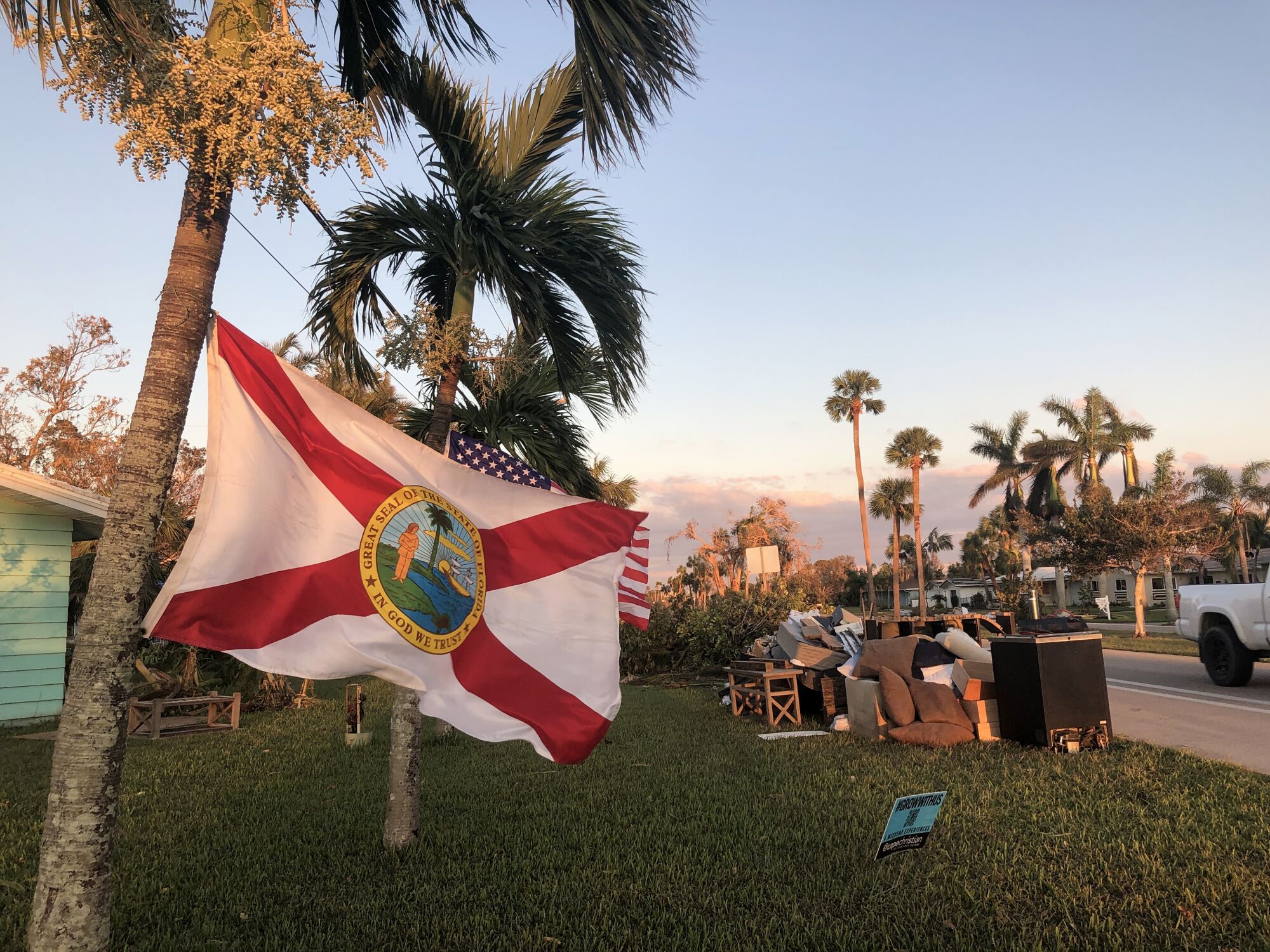 A Florida flag flies from a tree, with items from a home stacked behind