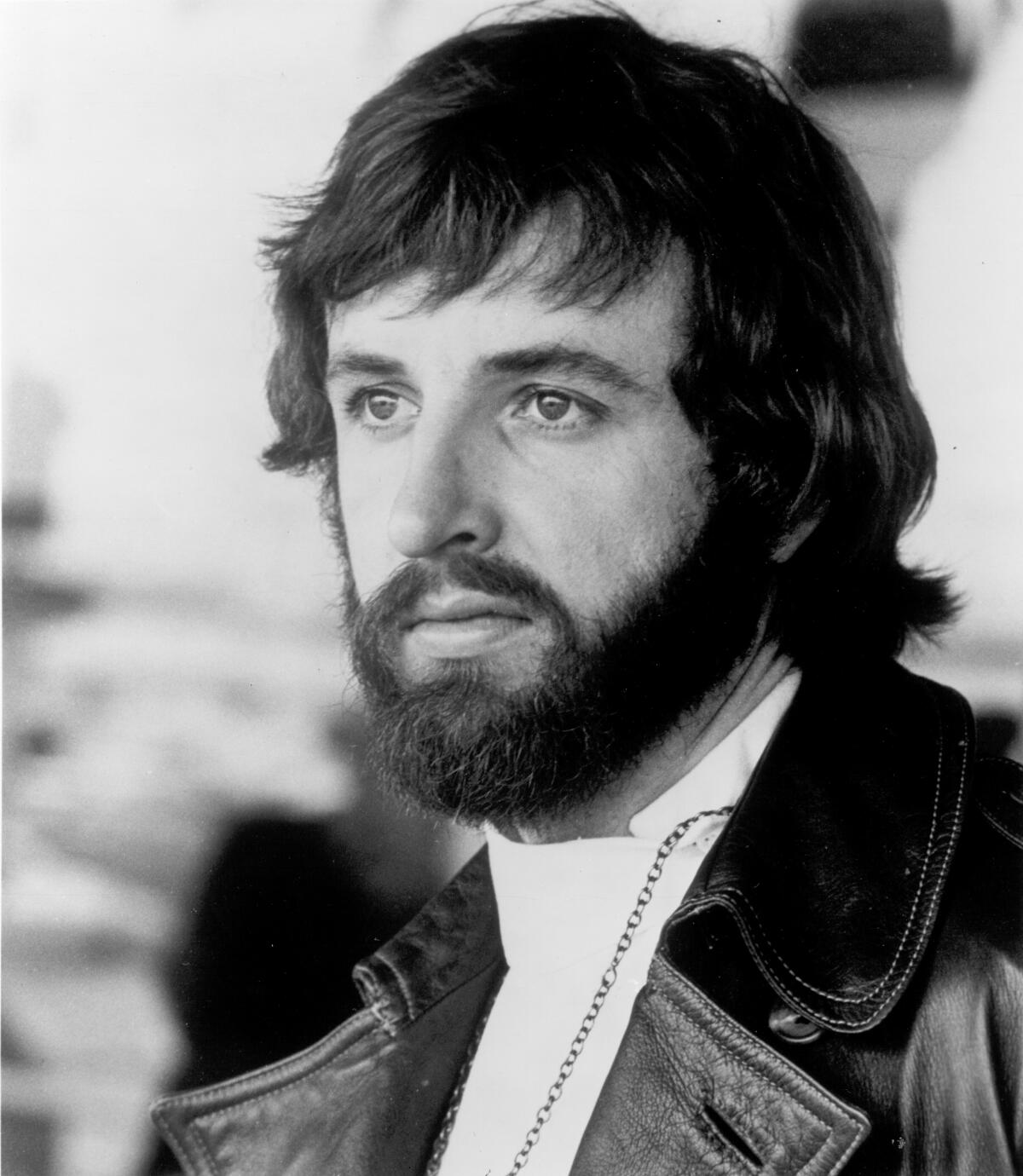 Photo portrait of Terry Kirkman staring off into the distance while wearing a leather jacket and Nehru collar shirt.