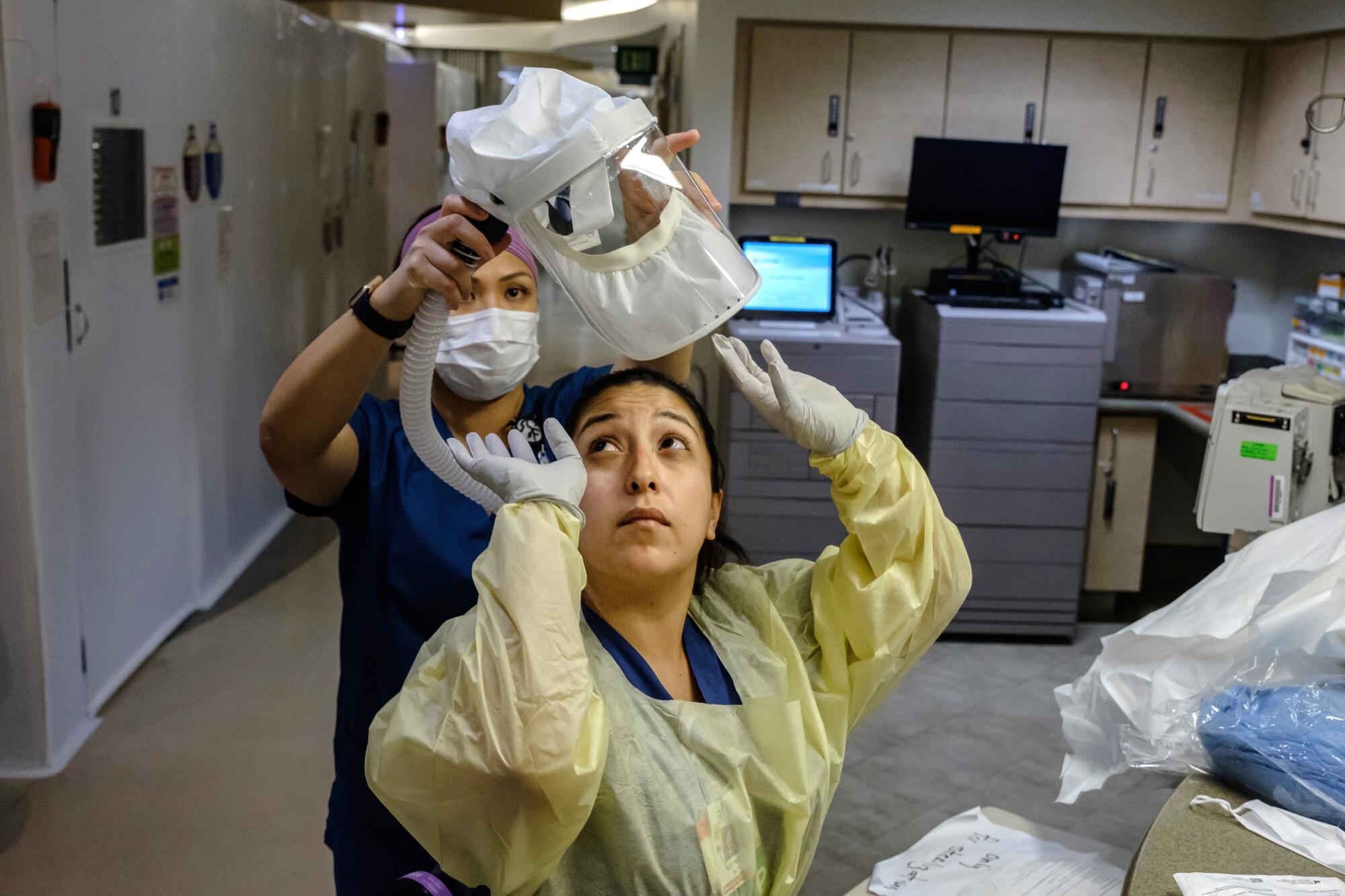 A woman in a mask helps another woman to put on protective headgear.