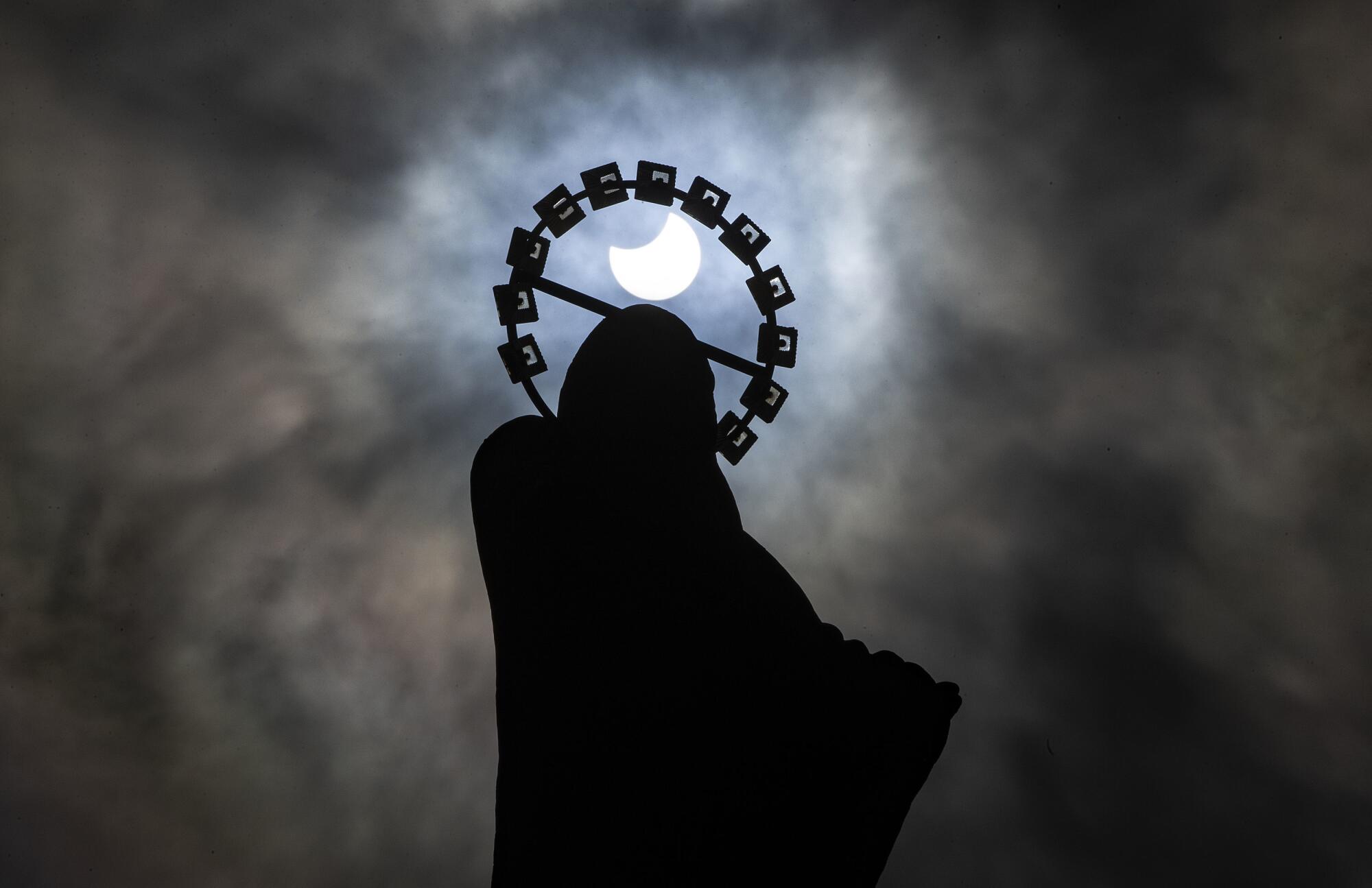 A statue of Our Lady, Star of the Sea on Bull Wall in Dublin, is silhouetted against the sky during partial eclipse.