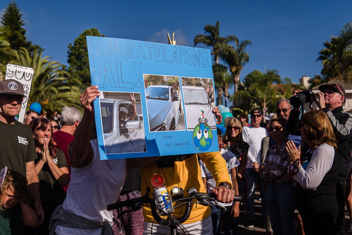 A woman holds a sign "Congratulations Al" in front of her and Al Merritt, 83, after his long bicycle ride.