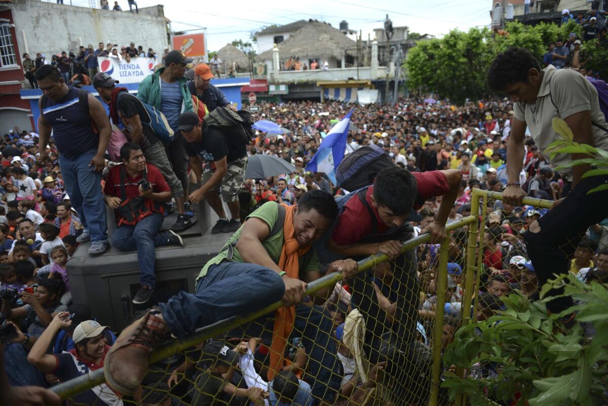 Miles de migrantes hondureños cruzan la frontera hacia México, en Tecún Umán, Guatemala, el jueves 18 de octubre de 2018. Los migrantes rompieron las puertas en el cruce fronterizo y comenzaron a correr hacia un puente en México. Después de llegar a la cerca alta de metal amarillo, algunos se subieron a ella y a jeeps militares donados por Estados Unidos. Los jóvenes comenzaron a tirar violentamente la barrera y finalmente lograron derribarla.