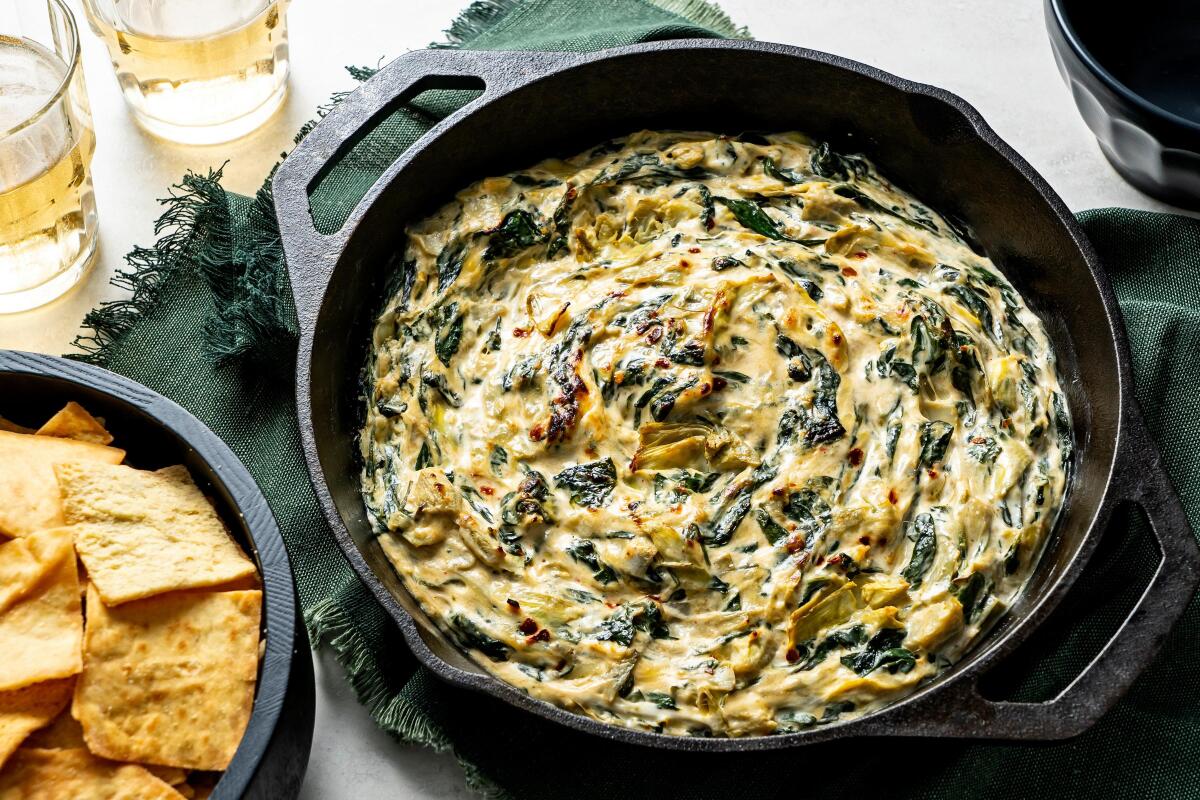 Spinach artichoke dip in a cast-iron pan sits on a table next to pita chips.