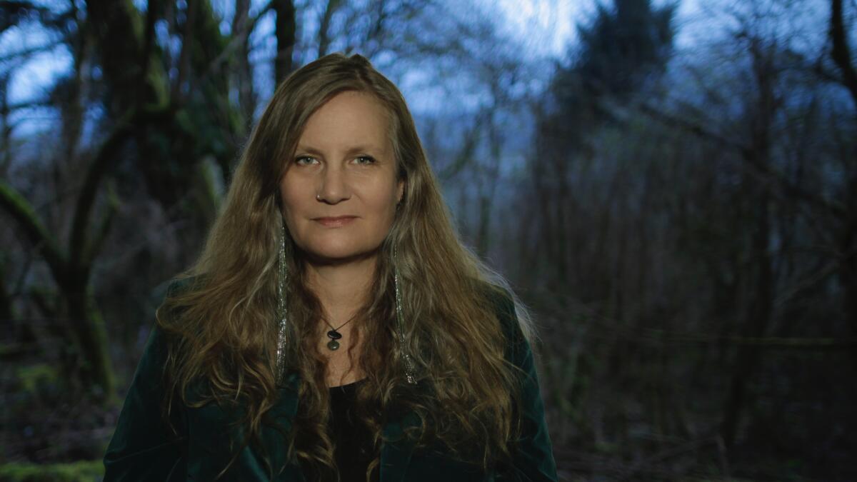 A woman stands in front of a forest.