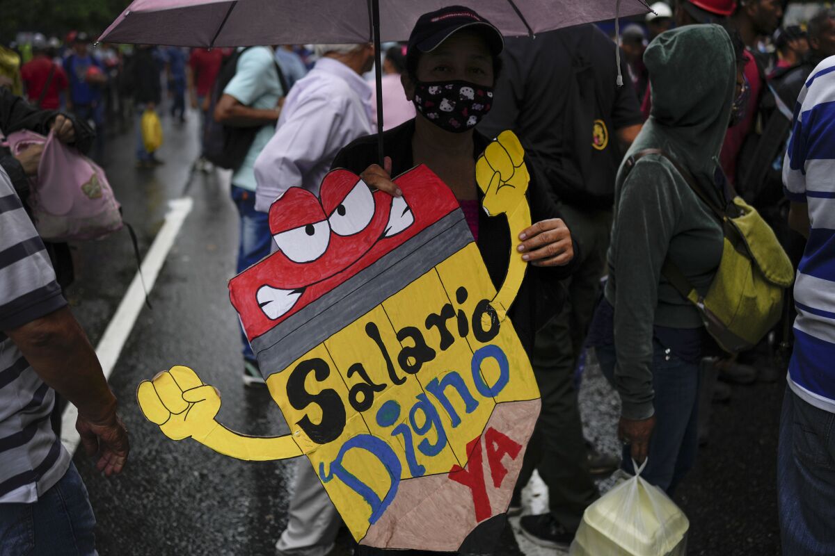 FILE - A teacher holds a sign that reads in Spanish: "Living wage now!" during a pro-government protest by public workers demanding the government pay their full benefits and respect collective bargaining agreements in Caracas, Venezuela, Wednesday, Aug. 10, 2022. (AP Photo/Matias Delacroix, File)