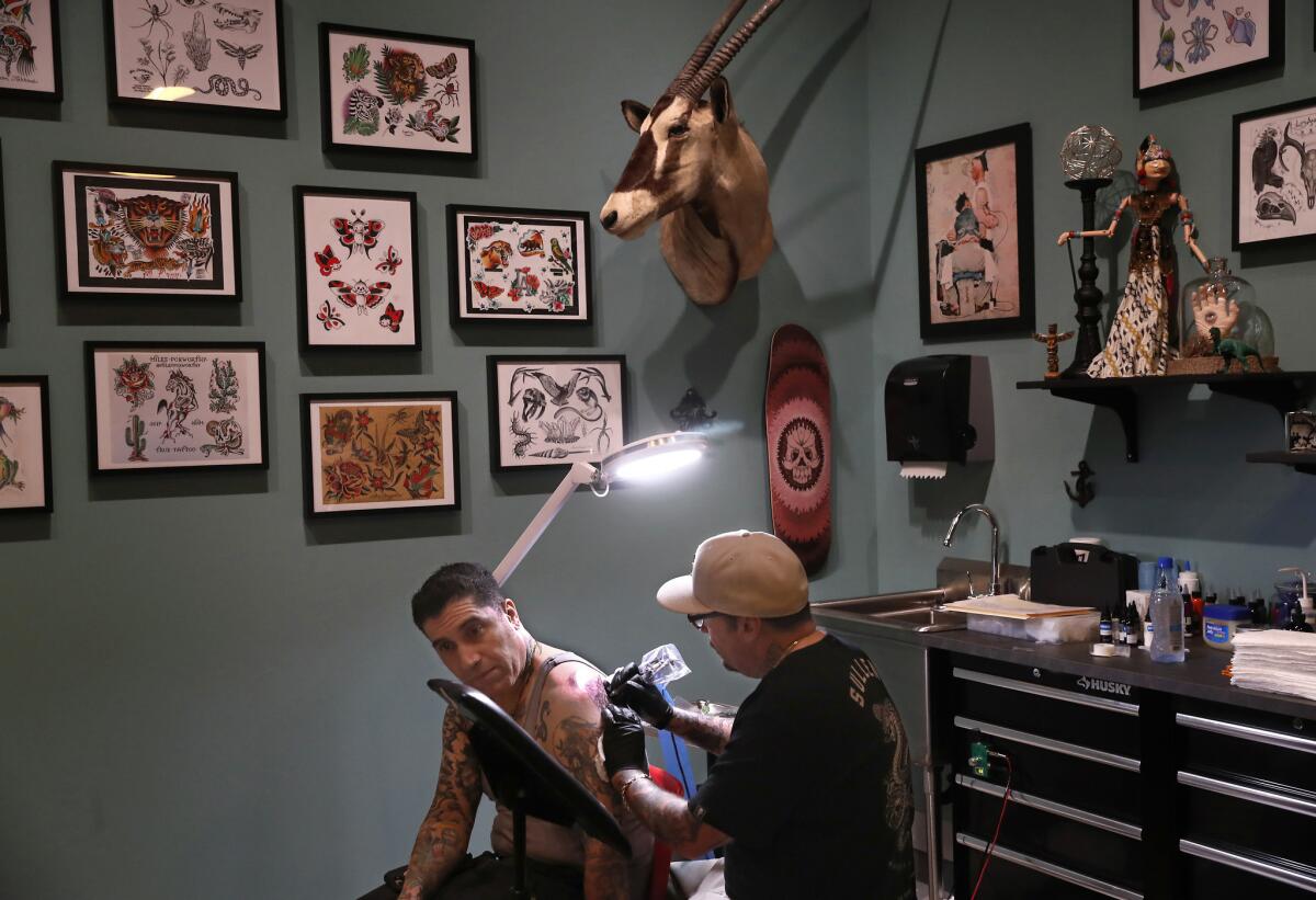Freddy Negrete applies a black-and-gray style tattoo to Louie Perez III inside the tattoo parlor set up at the Natural History Museum.