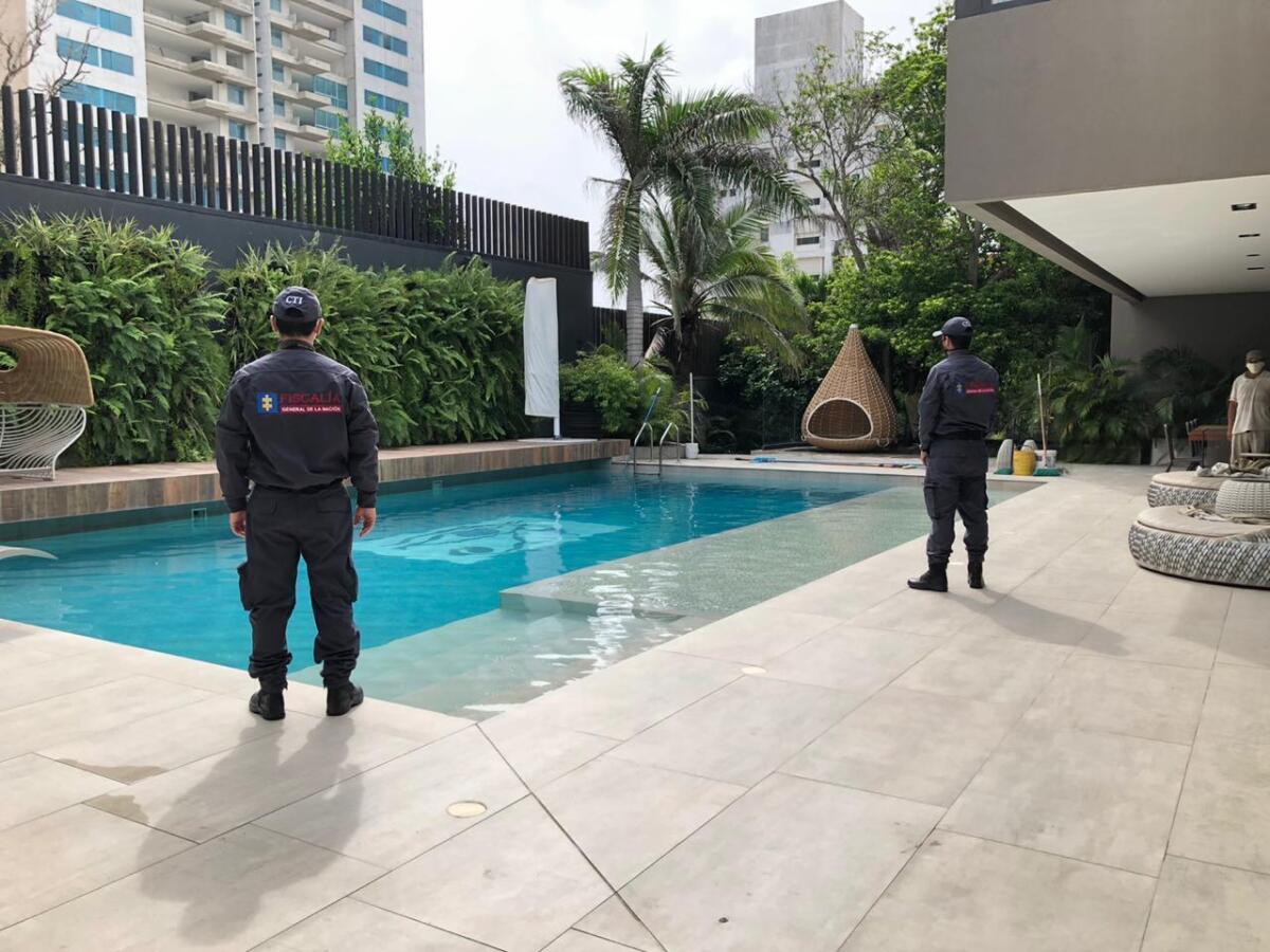 In this photo distributed by Colombia's Attorney Generals Office, officials pose with their backs to the camera by a pool on a property allegedly belonging to Alex Saab in Barranquilla, Colombia, Wednesday, July 22, 2020. Authorities seized a luxury mansion allegedly belonging to the businessman detained in Cape Verde on U.S. corruption charges related to Venezuelan President Nicolás Maduro. (Colombia's Attorney Generals Office via AP)